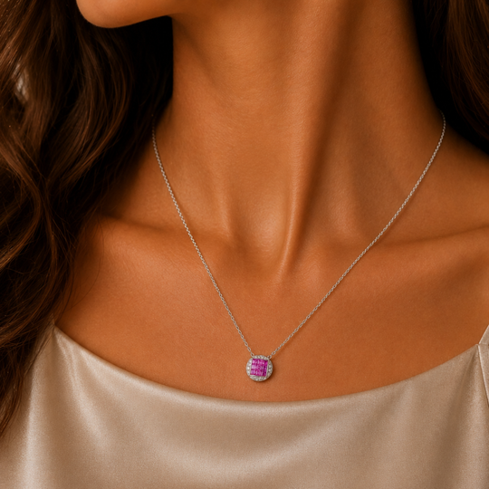 Pink Sapphire and Diamond 18ct White Gold pendant on lady's neck. She wears a soft satin scoop top. The pendant is round with a square of 9 pink saphires in the middle and the outside filled in with 16 smaller diamonds. It is shown on a white gold chain which can be purchased separately.
