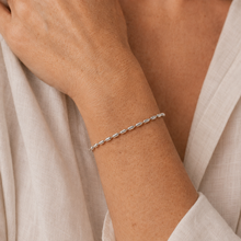 Load image into Gallery viewer, A delicate silver chain bracelet with small oval links, worn on a person's wrist. The person is wearing a light beige linen robe, and the background is softly blurred.
