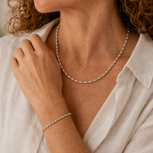 Load image into Gallery viewer, A close-up lifestyle shot of a woman wearing a delicate silver beaded chain necklace and a matching silver beaded bracelet, styled with a white linen shirt.
