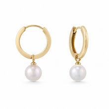 Load image into Gallery viewer, A pair of gold huggie hoop earrings with a single white freshwater pearl dangling from the bottom, shown against a plain white background.

