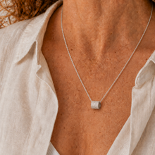 Load image into Gallery viewer, A close-up of a woman wearing a delicate silver chain necklace with a small textured cylindrical pendant, styled with a white linen shirt.

