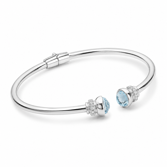 A polished silver-tone bangle bracelet with two light blue gemstone accents, each surrounded by small clear stones, shown on a clean white background.